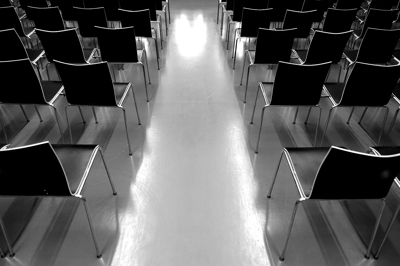 Rangées de chaises vides dans une salle de conférence, vues depuis l'allée centrale